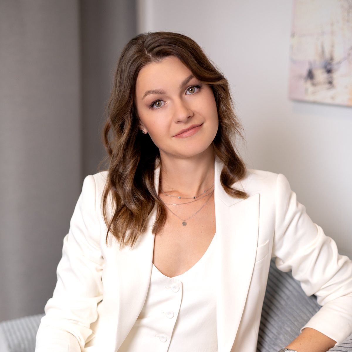 Natalia in a cream suit, sitting on a sofa and smiling